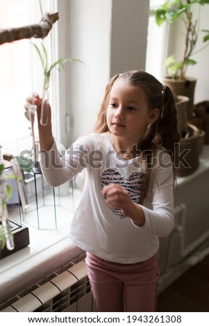 enthusiastic cute little girl in a white t-shirt with braids holding a test tube in her hands