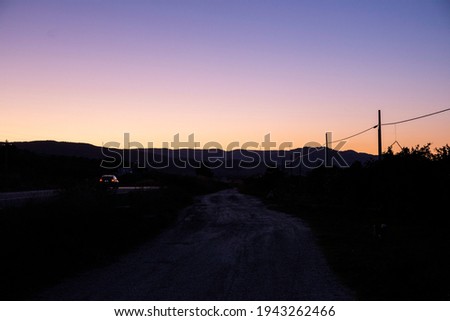 Dark gradient violet and yellow sunset with mountains in the background.