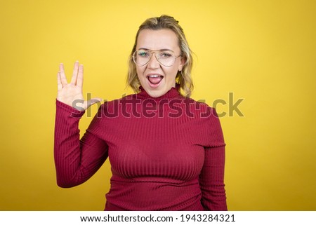 Young caucasian woman wearing casual red t-shirt over yellow background doing hand symbol