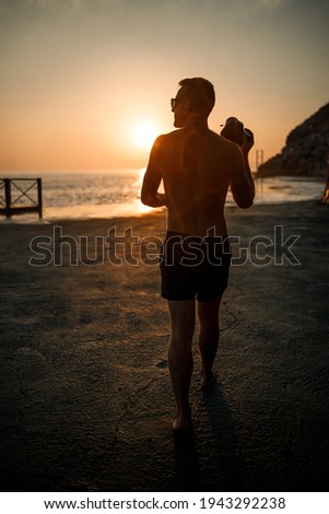Young male photographer makes photographs of the sea at sunset while standing on the shore. Sea sunset. Selective focus. Tourist photographs the seascape