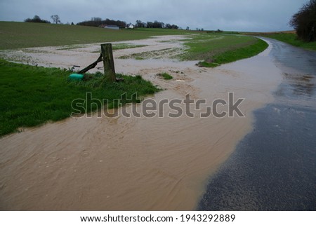Flash flood: excess rain water flowing off saturated agricultural land onto a public highway Royalty-Free Stock Photo #1943292889