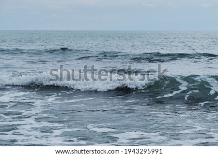 Beautiful blue sea waves with white foam close up. Bustling, violent ocean and horizon in background with cloudy, stormy sky. Minimalistic picture of sea landscape.