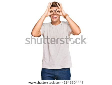 Handsome caucasian man wearing casual clothes and glasses doing ok gesture like binoculars sticking tongue out, eyes looking through fingers. crazy expression. 