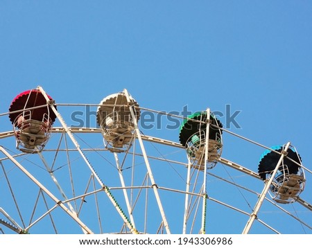 Fragment of a Ferris wheel with multi-colored cabins against a clear blue sky.