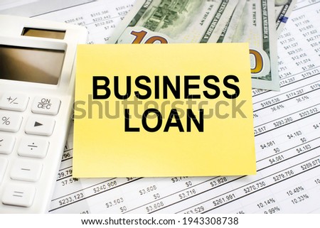 On the financial document next to a white calculator and dollars there is a yellow sheet on which the inscription business credit is written in black font.