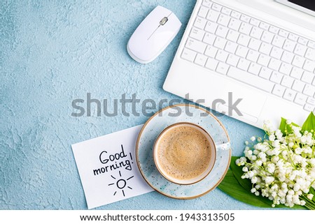 Home desk with notes good morning, coffee cup, bouquet of spring flowers lily of the valley. Workplace in home office with laptop. Breakfast, morning coffee, card, blogging, freelance concept
