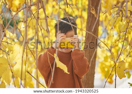 Little boy photographer playing under a yellow tree