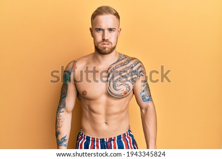 Young caucasian man wearing swimwear shirtless puffing cheeks with funny face. mouth inflated with air, crazy expression. 