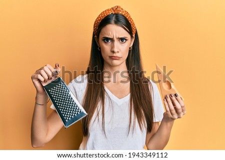 Beautiful brunette young woman holding grater and cheese skeptic and nervous, frowning upset because of problem. negative person. 