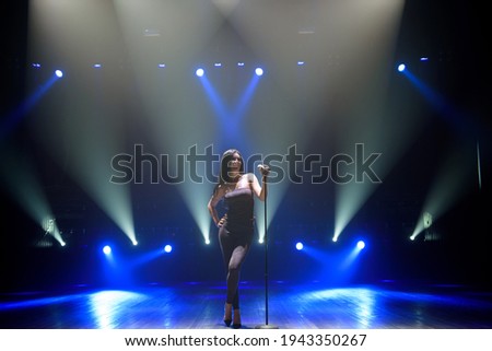 Pop musician with microphone singing a song on the stage in blue light background.