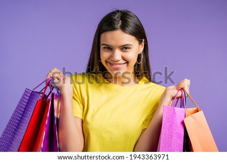 Excited woman with colorful paper bags after shopping on violet studio background. Concept of seasonal sale, purchases, spending money on gifts