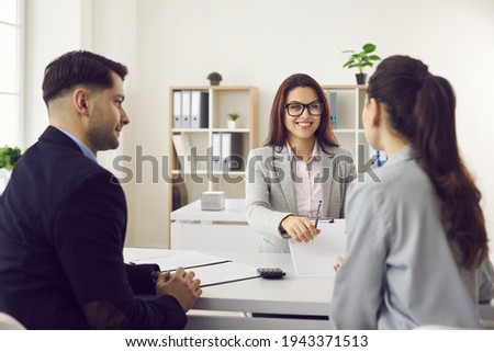 Smiling bank worker, real estate manager giving pen to sign contract promising good deal to woman client. Happy family couple customer and broker agent meeting for invest agreement signing in office