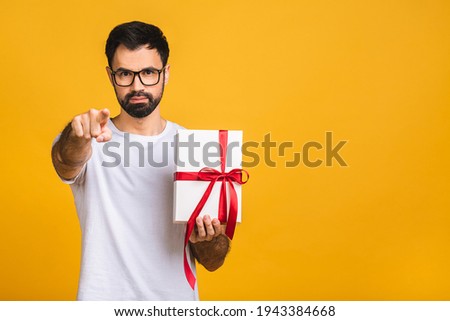 Wonderful gift! Adorable photo of attractive bearded man with beautiful smile holding birthday present box isolated over yellow background.