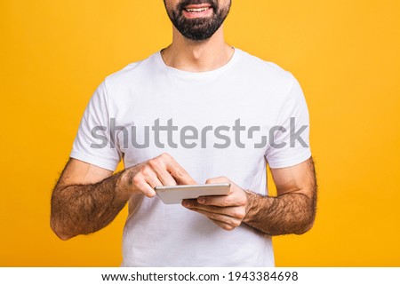Happy young bearded man in casual standing and using tablet isolated over yellow background. Close-up.