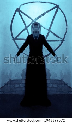 girl stands near the gray wall with painted pentagram in round.  Woman in long black dress. hands up. back, rear view.