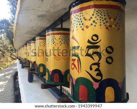 Outdoor perspective shot of a row of yellow Tibetan Buddhist prayer wheels decorated with colourful symbols meaning “Praise to the Jewel in the Lotus” on the path around the Dalai Lama temple, India