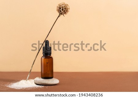 dropper bottle made of brown glass on brown background, still life with stone and dried flower
