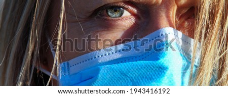 Close up of blonde woman with blue eyes with face mask, frowning expression.