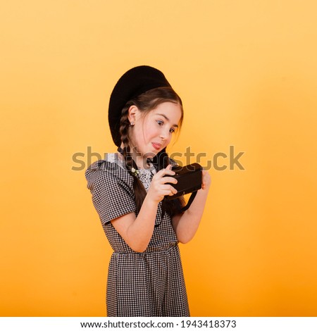 Portrait of baby girl holding photo camera isolated on a yellow background