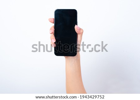 Woman's hand with pink manicure and long nails holding a telephone with blank empty screen for your images, message or text copy space over white studio background. Clipping path inside