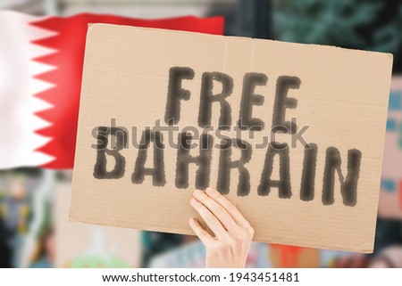 The phrase " Free Bahrain " on a banner in men's hand with blurred Bahraini flag on the background. Protest. Riot. Violence. Economic crisis. Collapse. Politics. Streets. Save. Cruelty