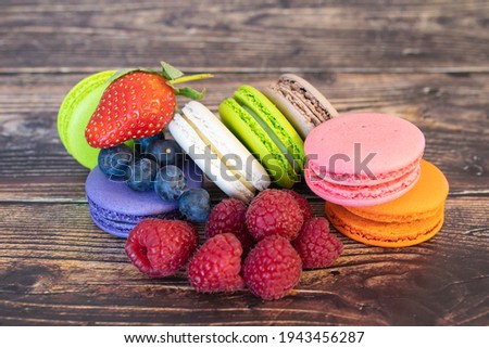 Delicious macaroons and wild berries, blueberries and raspberries on a wooden background.