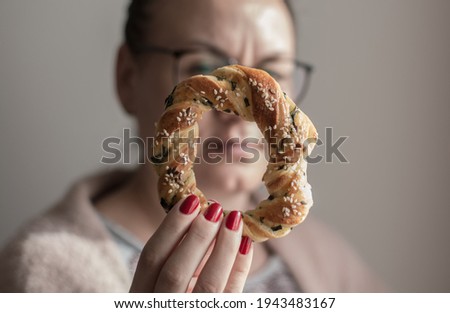 Woman with glasses in casual wear holding a bagel with sesame in her hand. Shallow depth of field. 