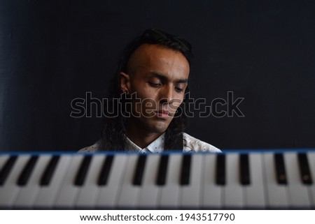 Conceptual music photography, keys of piano in the foreground with a musician in the background with a peaceful expression, close up