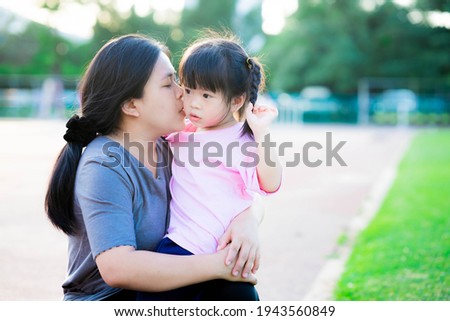 Mother embraced her touchy daughter and kissed her cheek. Family that understands each other. Warm family. Adult consoled the little girl. Asian child is 4 years old. Kids wears pink shirt in summer.