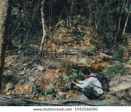 Young man photographer shooting near stream in forest