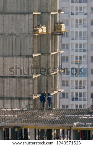 Two workers on the roof of a building under construction looking down against the background of the building