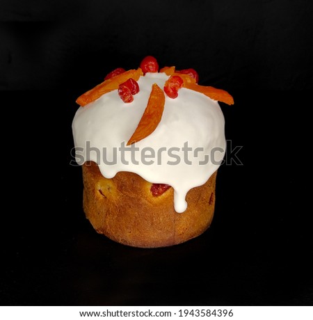 A sugar icing bun with dried apricots, raisins, candied fruits on dark background