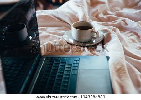 White cup of coffee  and laptop on the bed in morning time with soft light from window , low key