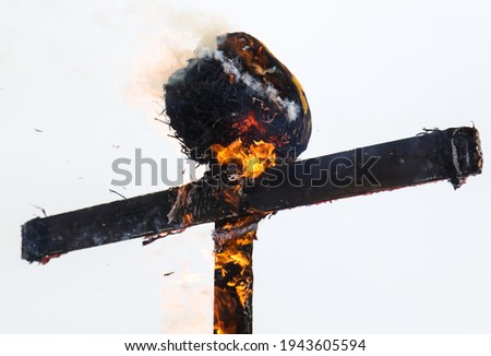 A wooden cross is burning with fire against a gray sky.