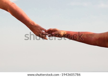 Hands of a man and a woman against a blue sky.