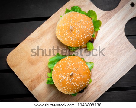 Delicious fresh homemade burger top view. Two tasty homemade hamburgers on wooden tray or wood cutting board on dark background.