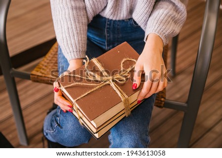 A stack of books lies on the young woman's lap.The books are tied with string. The girl is wearing a sweater and jeans. Student and schoolboy. Books from the library.Textbooks close-up.