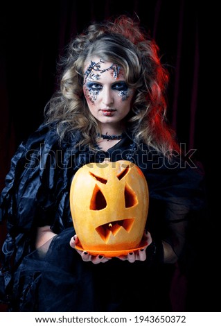 Young beautiful woman in a witch costume with bright makeup and hairstyle holding a pumpkin, a symbol of halloween. Party. Holiday. Carnival.