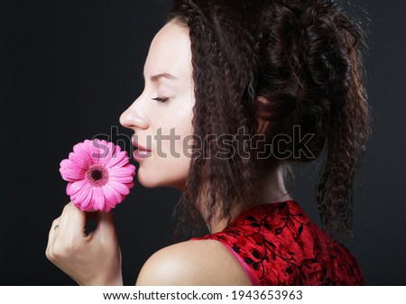 Young beautiful woman wearing red dress holding pink gerber flower. Close up.