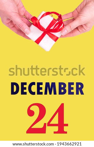 December 24th. Festive Vertical Calendar With Hands Holding White Gift Box With Red Ribbon And Calendar Date 24 December On Illuminating Yellow Background. Winter month, day of the year concept.