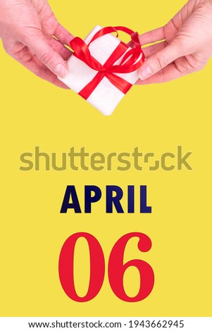 April 6th. Festive Vertical Calendar With Hands Holding White Gift Box With Red Ribbon And Calendar Date 6 April On Illuminating Yellow Background. Spring month, day of the year concept.