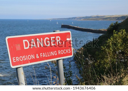 Danger sign warning of erosion and falling rocks on the sea cliff of St. Andrews in Scotland