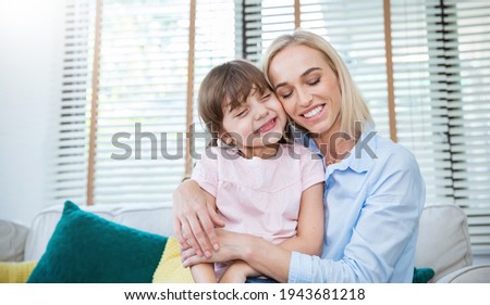 Portrait of happy caucasian mother and daughter. Caucasian woman little toddler girl cuddling and hugging in living room with copy space. Happy family spring or summer mother’s day together concept