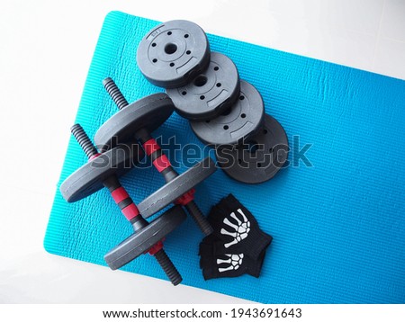 Dumbbells weight plates and gloveson a blue yoga mat, white background, copy-space dumbbells. Equipment to exercise to build muscle.​