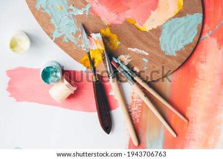 Palette with paints and brushes on colorful background, top view. 