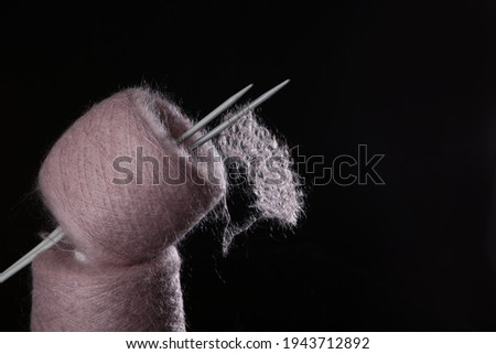 The concept of hobby knitting. The yarn is fluffy pink with knitting needles on a black background.Free space. Knitting on knitting needles. Natural wool mohair.Free space. 