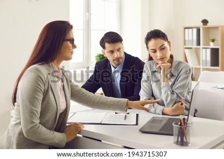 Office meeting with real estate agent. Couple of serious future buyers considering house variants and options on computer screen. Realtor helping clients take important decision and make right choice