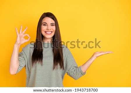 Portrait of attractive cheerful glad girl showing ok-sign holding copy empty space on palm isolated over bright yellow color background