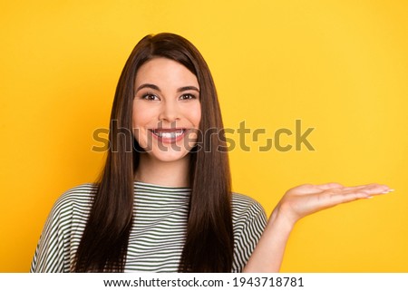 Photo of lovely adviser lady raise palm hold empty space toothy smile wear striped shirt isolated yellow background