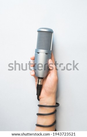 Male hand holding professional microphone on light background, top view. The microphone cable wrapped around hand. Vertical photo